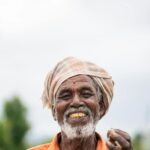 Elderly farmer smiling broadly, holding crops in a field. Rural lifestyle portrait emphasizing joy and tradition.